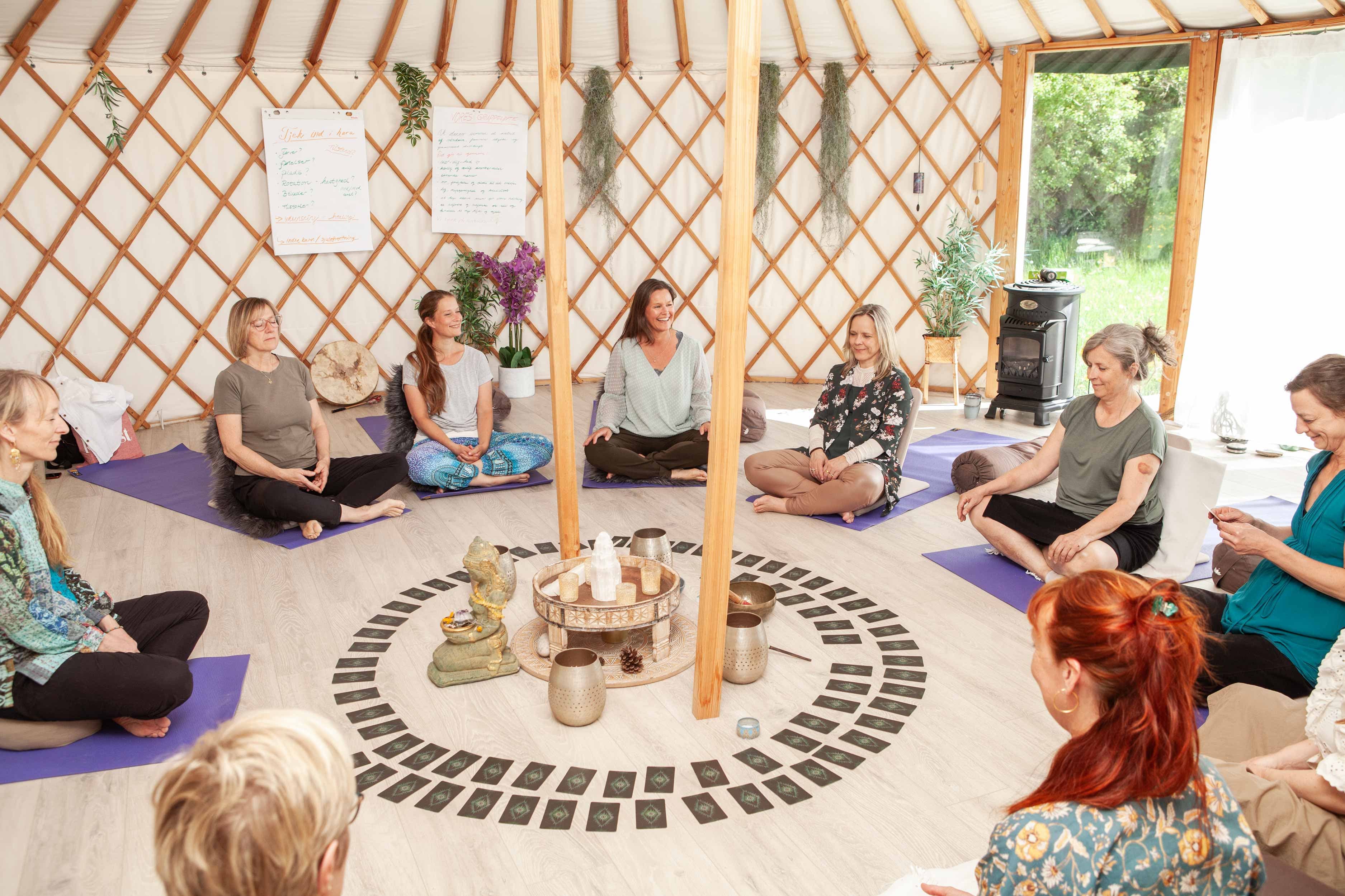 En kvindegruppe i en cirkel på yogamåtter med en smilende Lotte Weaver og krystaller i midten